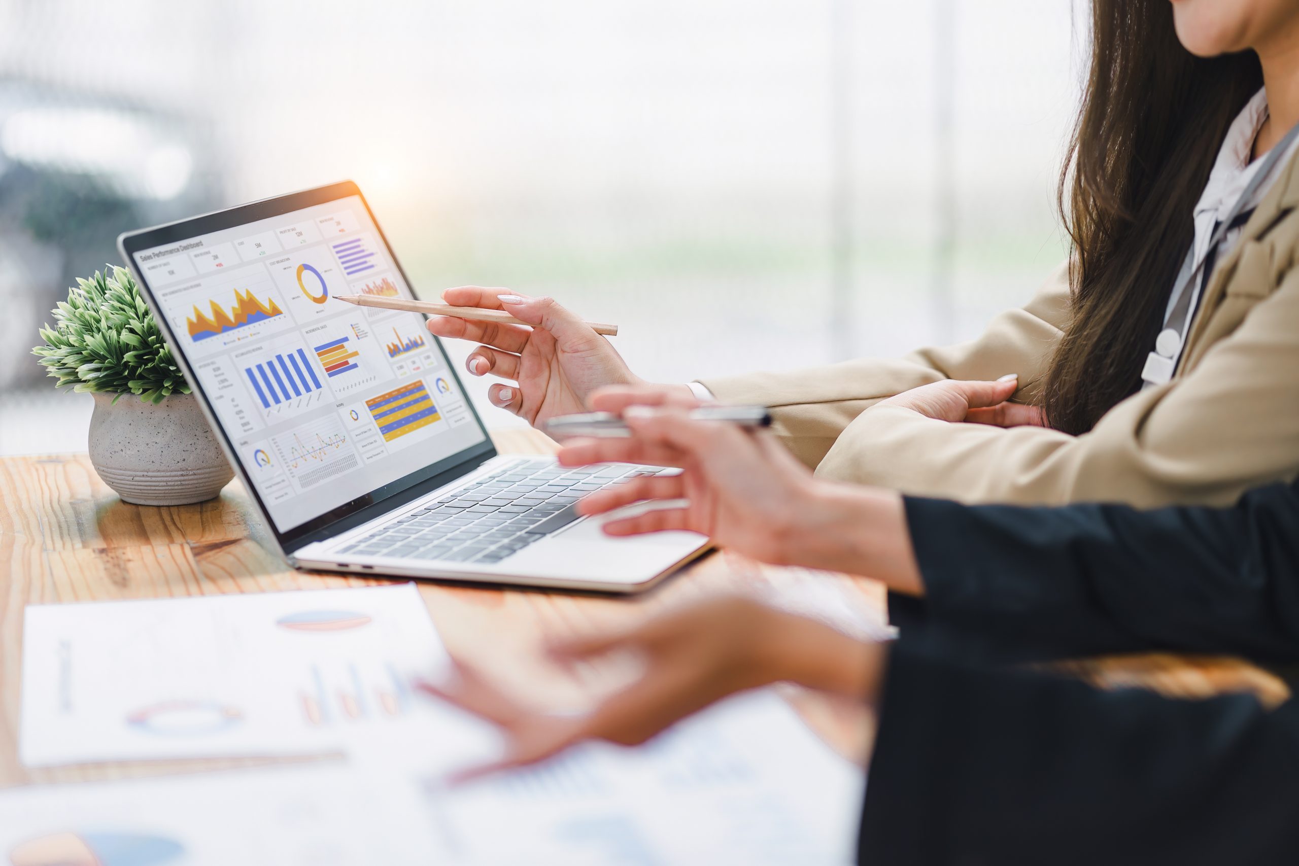 Two professional analyzing financial data graphs, charts on laptop display at a modern workspace. Financial analysis or business evaluation concept