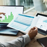 Hands, laptop and chart with paper for business man, analysis or check progress of economy, investment or profit. Financial agent, pc and reading graph for data document, growth or numbers for future